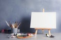 Easel with various artist tools on table against color wall Royalty Free Stock Photo