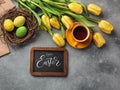Easter background with blue, green eggs and a cup of tea in nest and yellow tulips. Top view with copy space Royalty Free Stock Photo