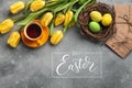 Easter background with blue, green eggs and a cup of tea in nest and yellow tulips. Top view with copy space Royalty Free Stock Photo