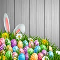 Easter background with bunny ears, flowers and colored decorated eggs in the grass on a wood background