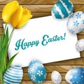 Easter background with colored eggs, yellow tulips and greeting card over white wood