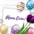 Easter background with colorful eggs, purple tulips and greeting card over white wood