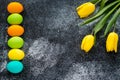 Easter background with copy space. Paschal gift card with painted eggs and yellow tulips on grunge dark black backdrop. Template,