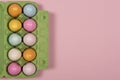 Easter background with a green carton egg box with pastel colored easter eggs in it on a pink background