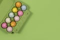 Easter background with a green carton egg box with pastel colored easter eggs in it on a green background with space for copy