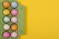 Easter background with a green carton egg box with pastel colored easter eggs in it on a yellow background