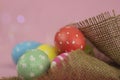 Easter background. Green, red and yellow painted eggs handmade in sackcloth on a pink background with bokeh. Royalty Free Stock Photo