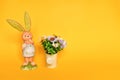 Easter background with small lovely rabit standing and colorful plastic flower in watering can on yellow background, decorate and Royalty Free Stock Photo