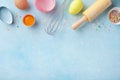 Easter baking background with rolling pin, whisk, eggs, flour and colorful confetti on blue table top view. Flat lay