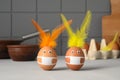 Two brown easter rabbits made from eggs wearing protective face masks and feather ears on the kitchen table