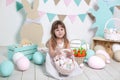 Easter! Beautiful little girl in a white dress lays Easter eggs in a basket. Many different colorful Easter eggs, colorful interio