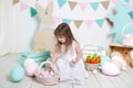 Easter! Beautiful little girl in a white dress lays Easter eggs in a basket. Many different colorful Easter eggs, colorful interio