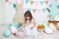 Easter! Beautiful little girl in a white dress lays Easter eggs in a basket. Many different colorful Easter eggs, colorful interio