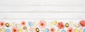 Easter bottom border with eggs, paper flowers and wooden bunnies over a white wood banner background