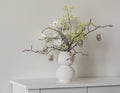 Easter bouquet of dry twigs, flowers, glass Easter eggs in a ceramic white vase on a white chest of drawers Royalty Free Stock Photo