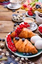 Easter breakfast flat lay with fresh coffee, berries and pastries , orange tulips, croissants with bacon and various sweets ,