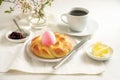 Easter breakfast for one, plaited yeast bread nest with a pink egg, coffee, butter and jam on a white table, during the