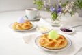 Easter breakfast with plaited yeast bread nests and colored eggs, coffee, butter, jam and flowers on a white table, copy space