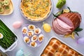 Easter brunch on large table with spiral sliced ham, quiche, deviled eggs and hot cross buns