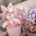 Easter bunnie in pink little bucket, next to a spring flowers. Home holiday composition