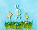 Easter bunnies figurines, painted eggs on green grass on blue background. Egg hunt creative concept Royalty Free Stock Photo