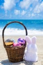 Easter bunny with basket and color eggs on the ocean beach