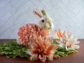 Easter Bunny Decor sitting on green leaves surrounded by peach artificial dahlia flower blooms, perfect for the spring holiday