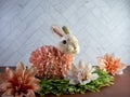 Easter Bunny Decor sitting on green leaves surrounded by peach artificial dahlia flower blooms, perfect for the spring holiday