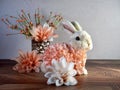 Easter Bunny Decor sitting on a wooden surface surrounded by peach artificial dahlia flower blooms, perfect for the spring holida