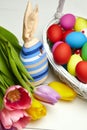 Easter bunny doll and Easter eggs in basket and spring colorful flowers on white wooden table Royalty Free Stock Photo