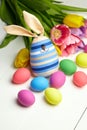 Easter bunny doll and Easter eggs in basket and spring colorful flowers on white wooden table Royalty Free Stock Photo