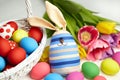 Easter bunny doll and Easter eggs in basket and spring colorful flowers on white wooden table Royalty Free Stock Photo