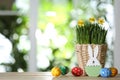 Easter bunny figure, dyed eggs and flowers on table against blurred green background. Space for text Royalty Free Stock Photo