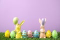 Easter bunny figures and dyed eggs on grass against violet background Royalty Free Stock Photo