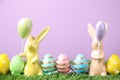 Easter bunny figures and dyed eggs on grass against violet background Royalty Free Stock Photo