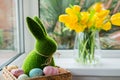 Easter bunny rabbit statuette in straw basket with colored eggs on the windowsill with fresh spring tulips and daffodils Royalty Free Stock Photo