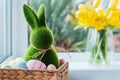 Easter bunny rabbit statuette in straw basket with colored eggs on the windowsill with fresh spring tulips and daffodils Royalty Free Stock Photo