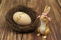 Easter bunny with a wicker nest and a wooden egg with a golden inscription