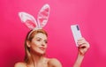 Easter bunny woman with rabbit ears having call holding smart phone in hand shooting selfie on front camera. Royalty Free Stock Photo