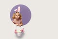 Easter card. Cute little child girl with bunny ears holding basket of Easter eggs. Child in a round hole circle in colored purple Royalty Free Stock Photo