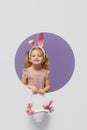 Easter card. Cute little child girl with bunny ears holding basket of Easter eggs. Child in a round hole circle in colored purple Royalty Free Stock Photo