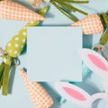 Easter carrots on a pastel blue background with square blank paper on top.