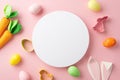 Top view photo of white circle colorful easter eggs bunny ears backing molds and carrots on isolated pastel pink background