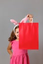 Easter. A cheerful little girl in a pink dress peeks out from behind a shopping bag. Cute child on  gray background Royalty Free Stock Photo