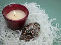 Easter colored egg and burning candle on white crinkle shredded paper