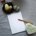 Easter decorated eggs in nest, blank paper notepad on grey background