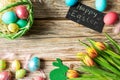 Easter colorful eggs in a basket, on a wooden table, with tulips top view, inscription Happy Easter