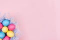 Easter colorful eggs in fun blue nest on soft pink background, copy space, top view.