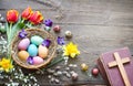 Easter colorful eggs in the nest with flowers on vintage wooden boards with bible and cross Royalty Free Stock Photo