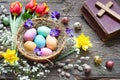 Easter colorful eggs in the nest with flowers on vintage wooden boards with bible and cross Royalty Free Stock Photo